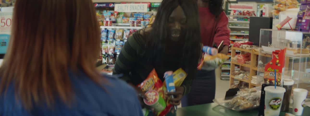 Two woman walk to the counter of a store with items in their arms