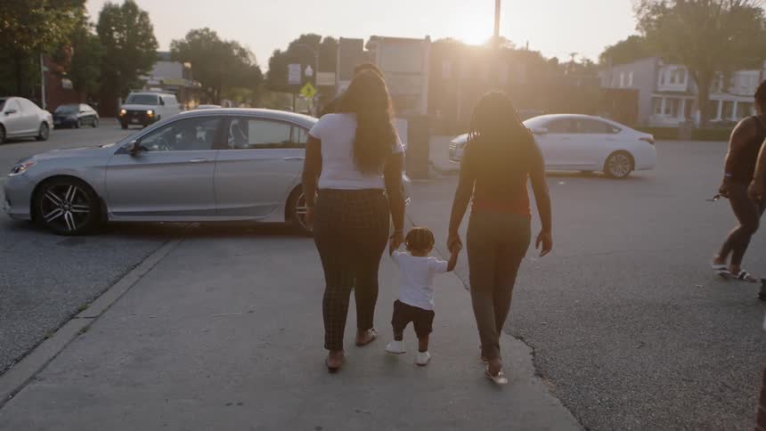 Two women picking up and swinging a baby walking down the sidewalk