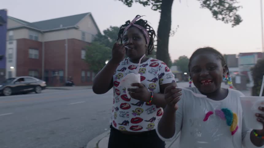 Two children carry cups and smile walking down the street