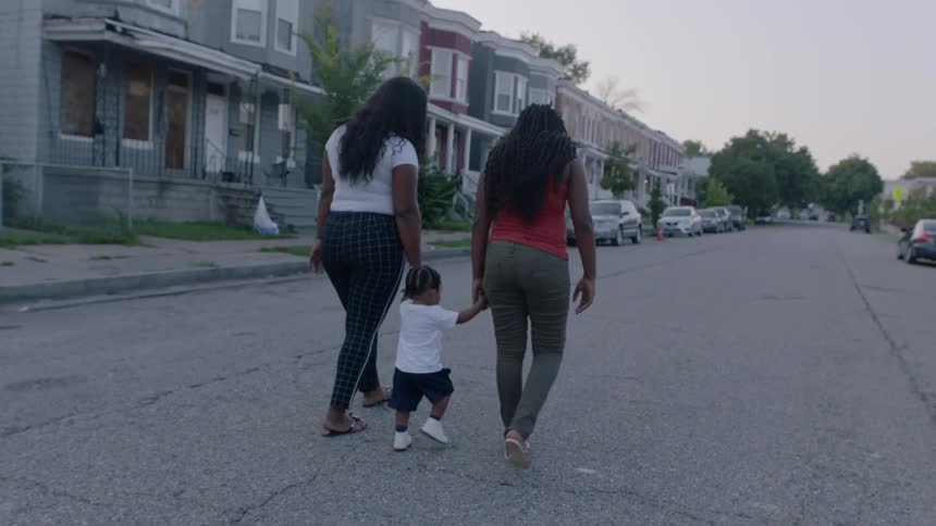 Two women and one child walking down a street in a neighborhood