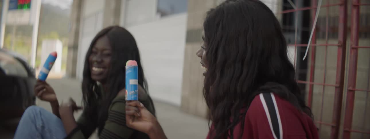 Two females eating a snack while sitting on a curb