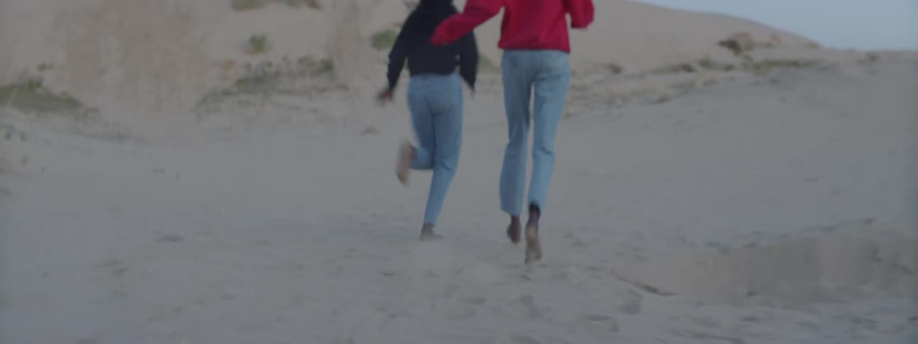 Two women in jeans running through the sand dunes