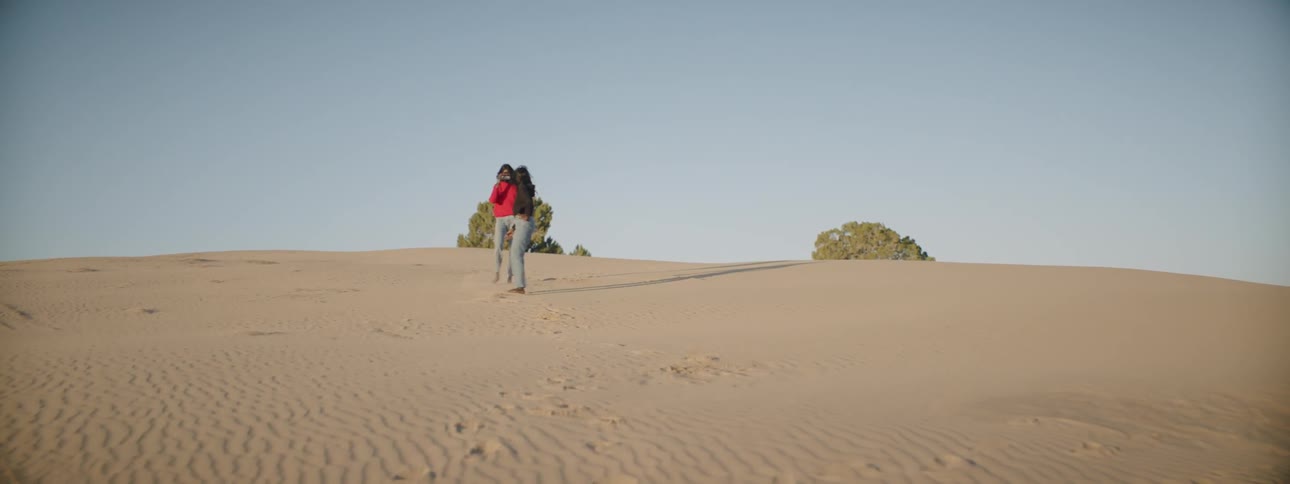 Two women walking and prancing along a large sandy area