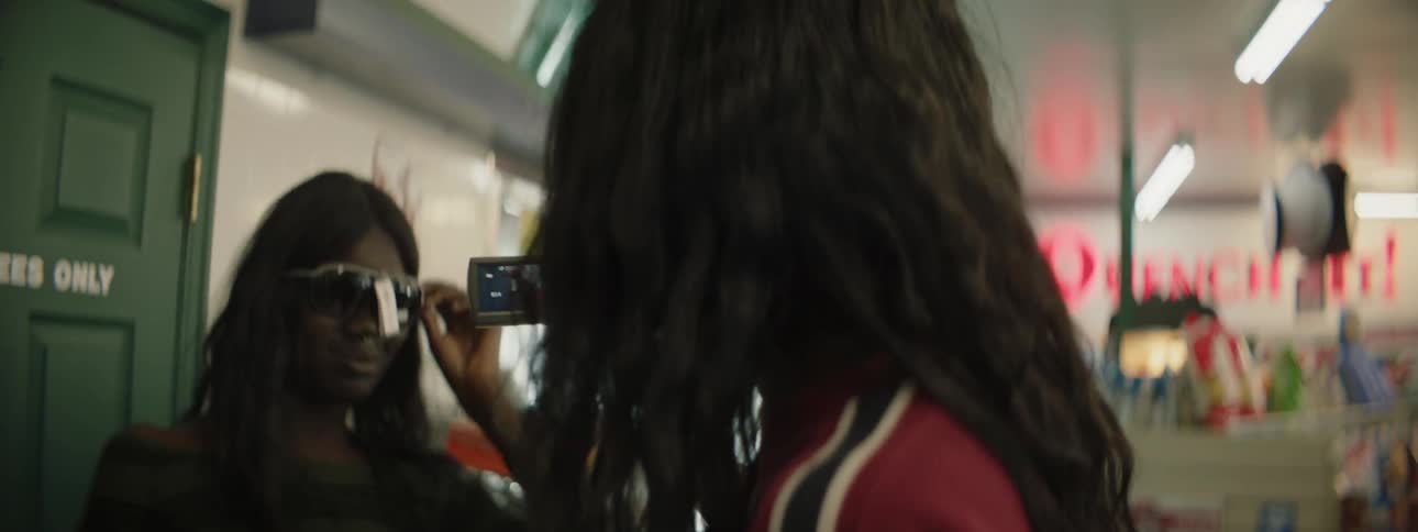 A woman wearing sunglasses with a price tag on them records another woman that is also wearing sunglasses with a price tag on them in a store