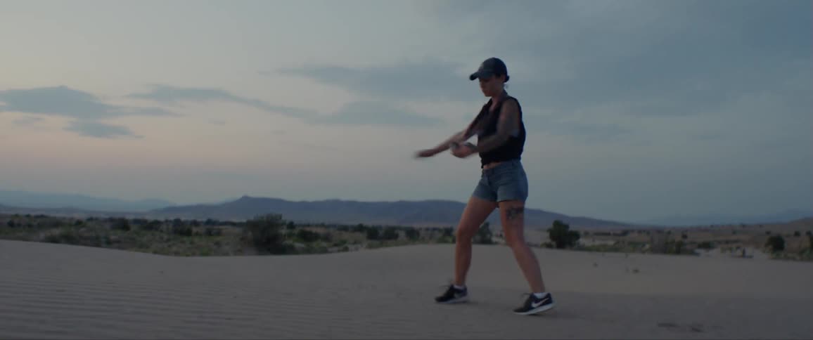A woman walks and skips and dances along a sand dune