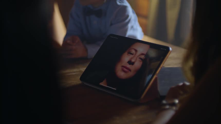 A group of people sit around a table talking to a woman on a video chat