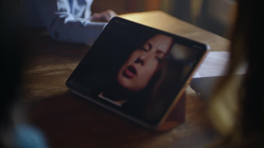 A woman on a video chat can be seen on a tablet as a child plays behind it