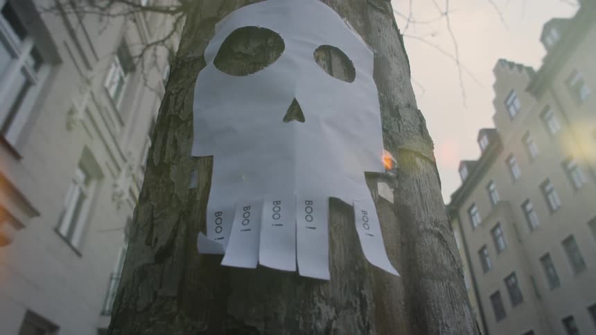 A paper shaped like a skull is stapled to a tree