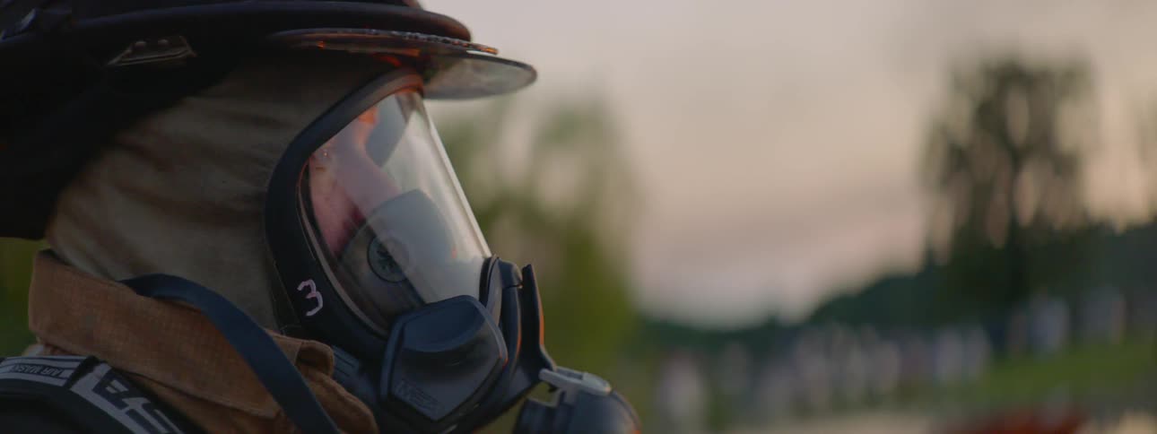 A fireman in full gear stands with trees in the distance behind him
