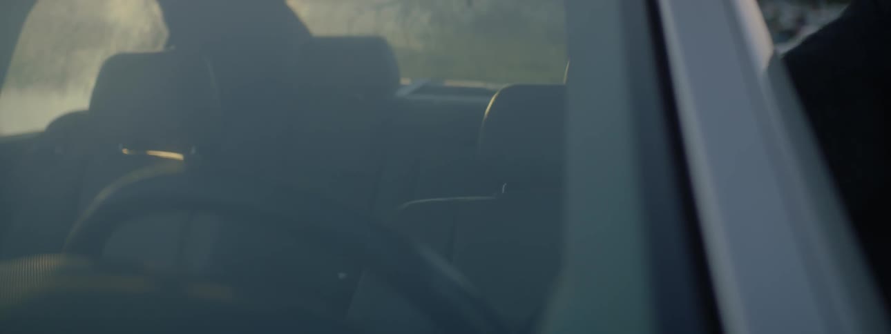 A man in a suit sitting in the driver's seat of a car and getting out of it