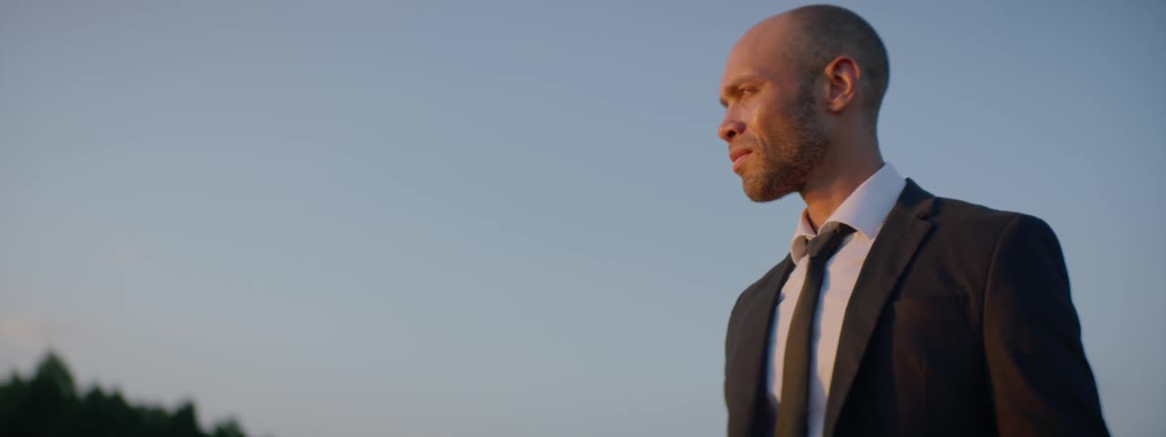 A man in a suit standing on the top of a hill looking into the distance