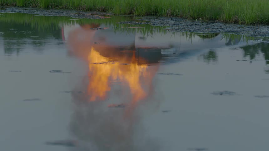 A reflection of a burning car can be seen in a river