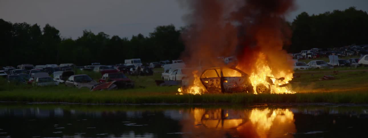 A car fire in the distance of a body of water near other cars