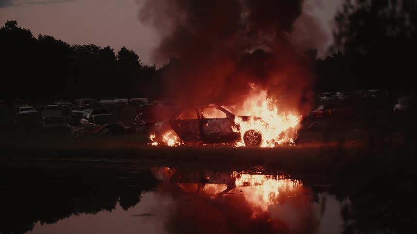 A car that is on fire at the edge of a lake