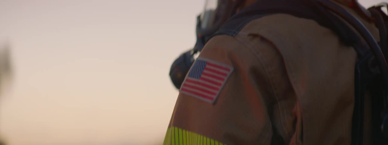 A fireman wears a fireman's mask while standing by the flashing lights at sunset