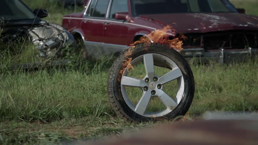 Burning wheel rolls through the grass in between rows of cars