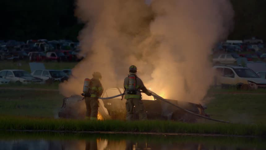 Two firefighters putting out a burning car