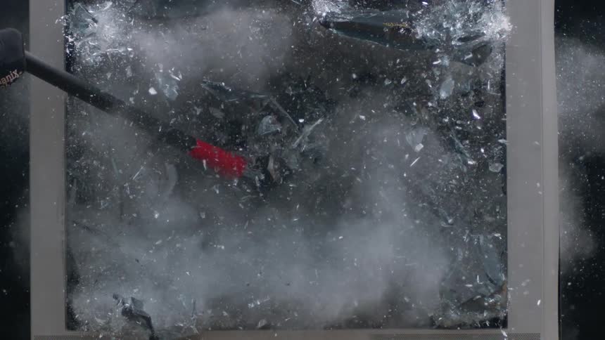 A person swinging a sledge hammer and breaking a glass panel