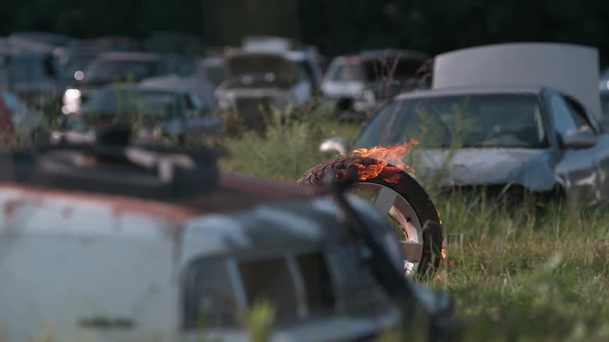 Burning wheel rolls through the grass in between rows of cars