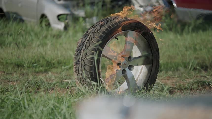 A tire on fire is rolling along the grass
