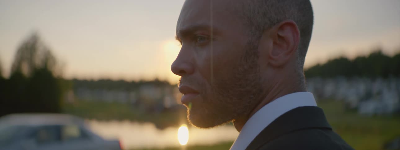 A man in a tuxedo stands and looks out at the sunset