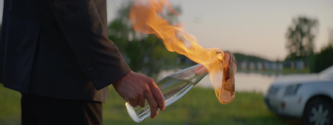 Man holds molotov cocktail and walks to a car