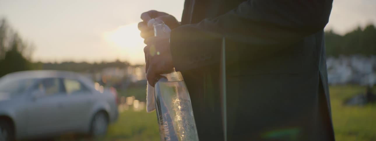 A man shoves a rag into a bottle in a junkyard