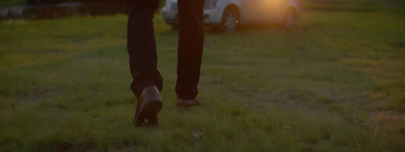 Person walks toward a car in a grassy field