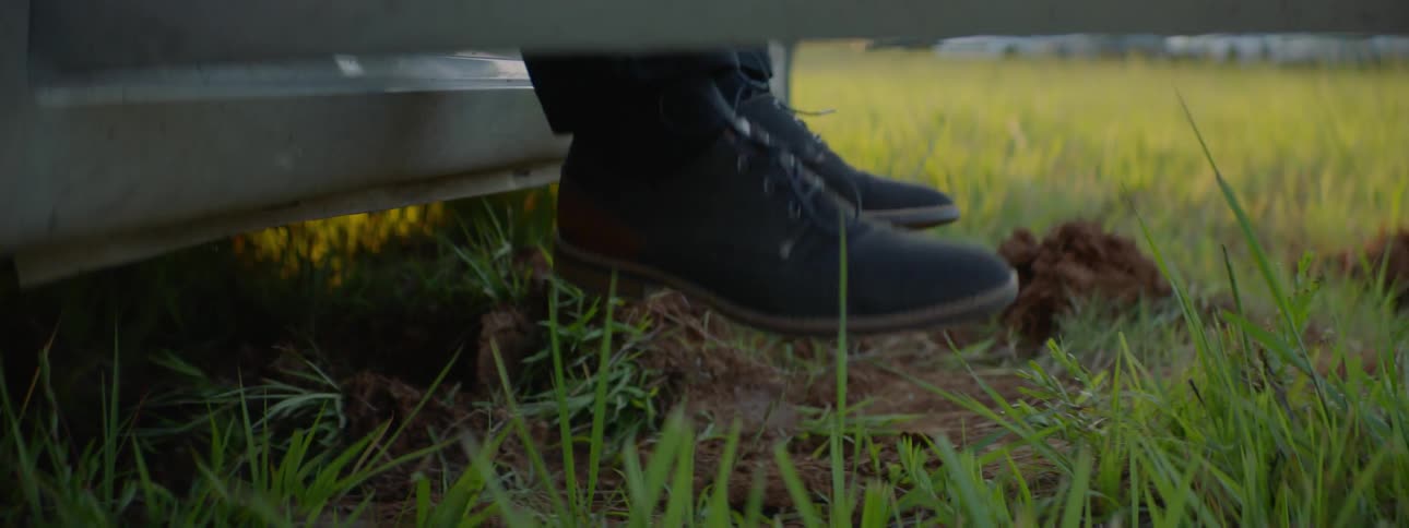 A man with dress shoes getting out of his car and stepping into a muddy field