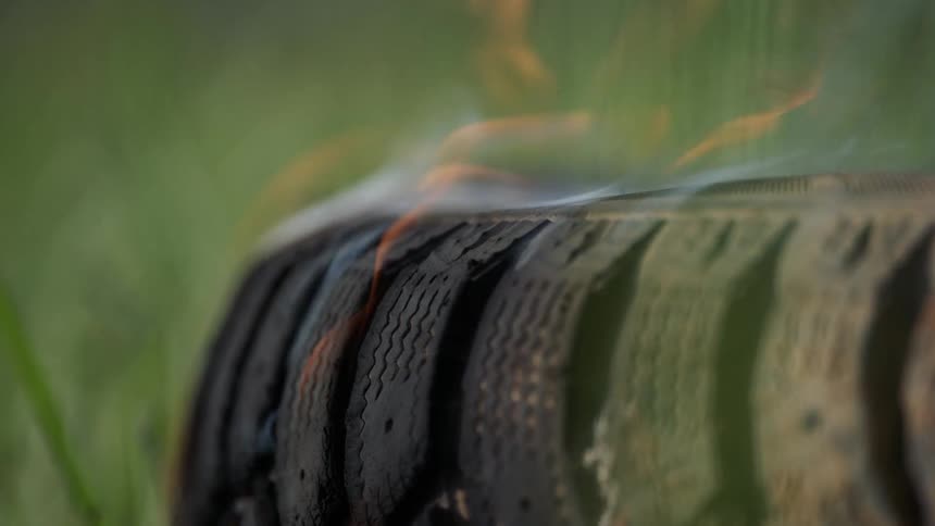 A tire in the grass is burning from a fire