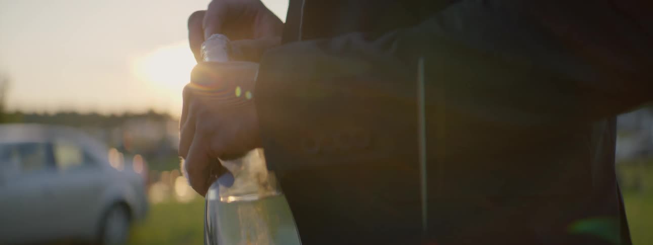 A man is holding a bottle in the sunlight