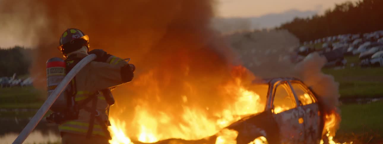 Firefighter trying to put out a burning car in a field