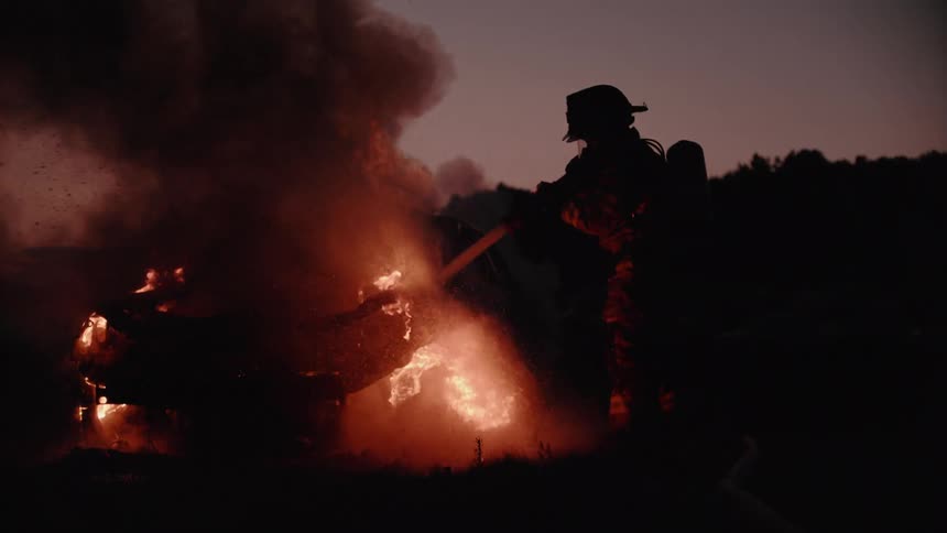 A fireman attempts to put out a fire that has engulfed a car