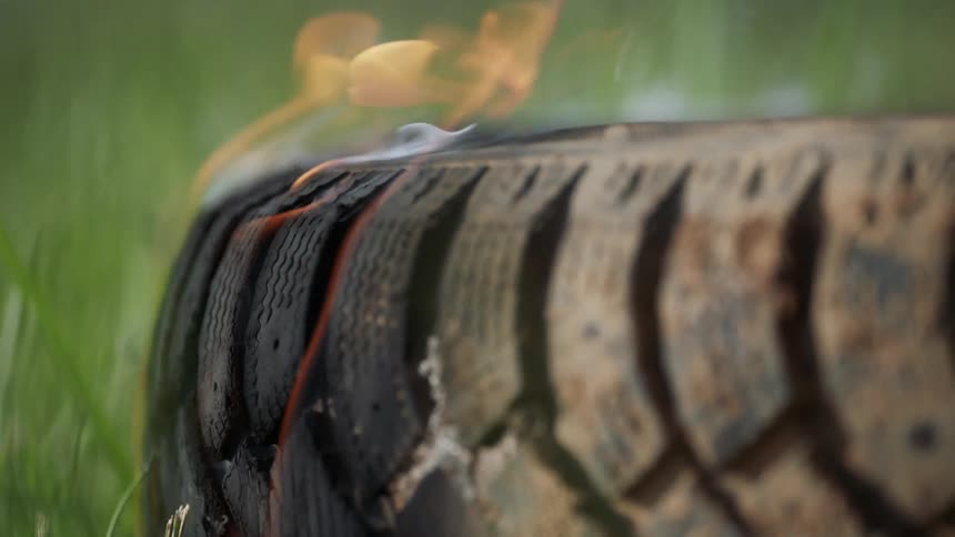 Flames are rippling off of a tire laying in the grass