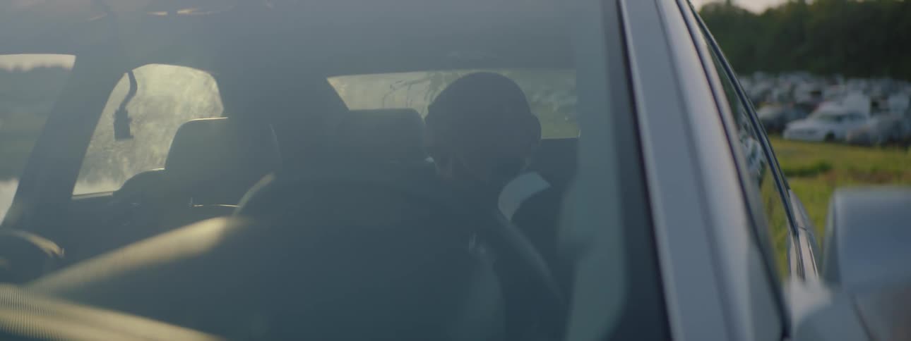 A man rubs his head in the driver seat of a parked car