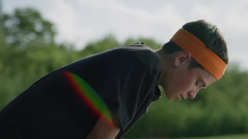 Boy standing in a field leans over breathing heavily