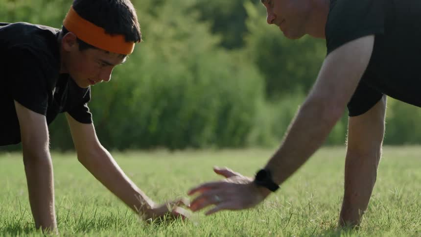 A man and a boy do push ups and touch hands each time they come up from one