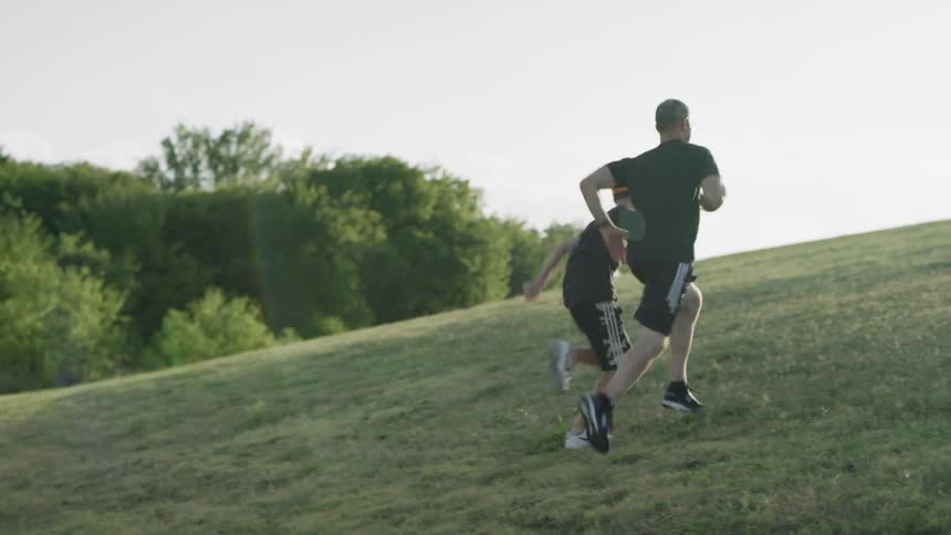 Two men run up a grassy hill