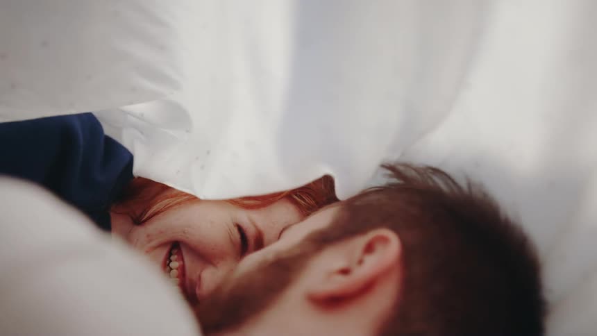 Woman and man laugh while laying under a sheet