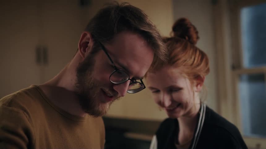 A man and woman stand inside a house talking and laughing