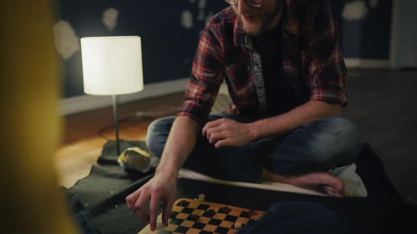 A man and woman play checkers together on a blanket on the floor