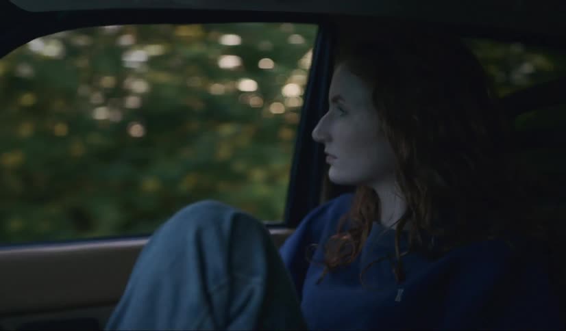 A woman sits in a car and puts her hand out the window
