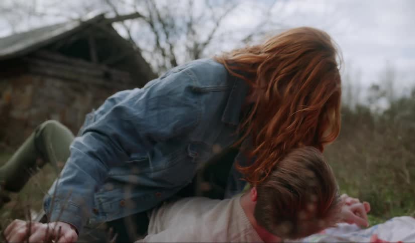 A man and woman wrestling and kissing on a blanket in a field