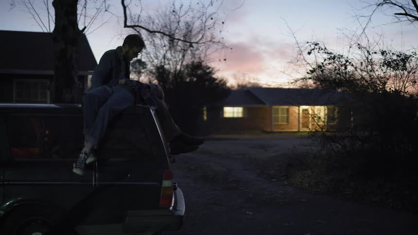 A man that is sitting in the bed of a truck outside of a house