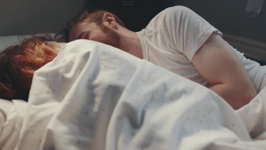 A man and woman are laying in bed together and kissing