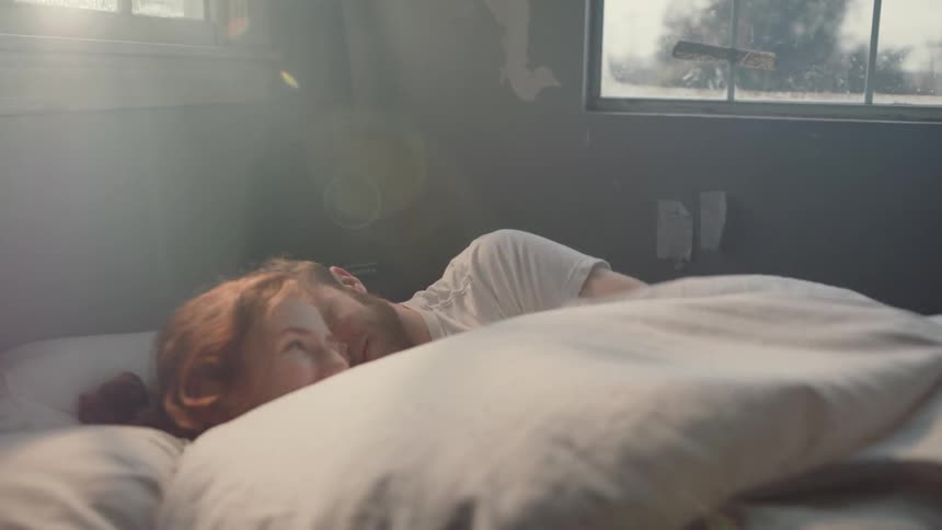 Man and woman snuggle under the covers on a bed