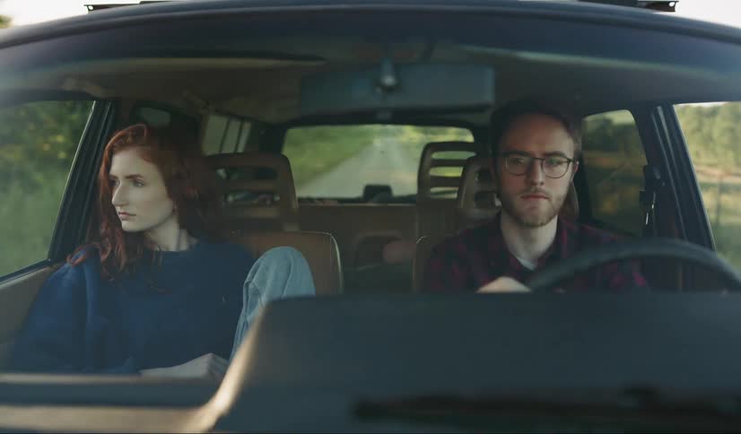 A man drives a car on a sunny day with a woman in the passenger seat