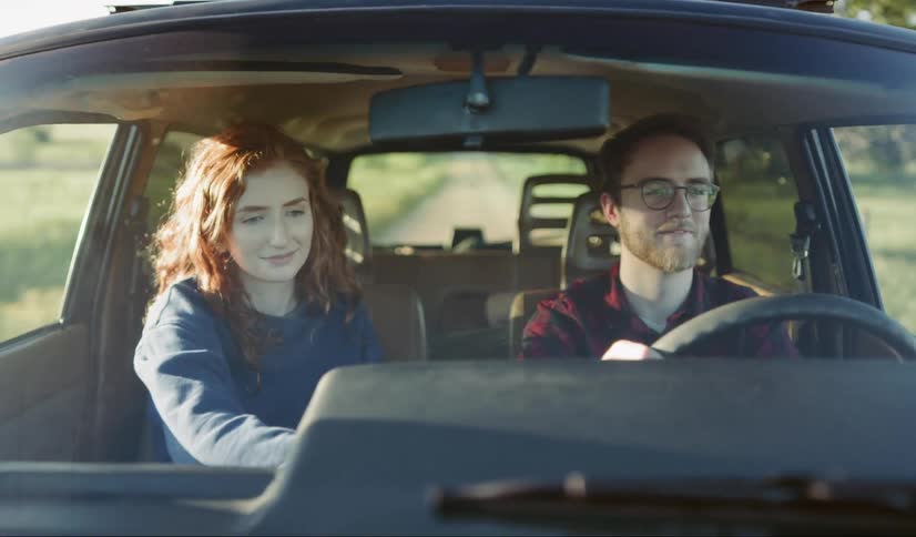 A man is driving a car, and the woman is smoking a cigarette