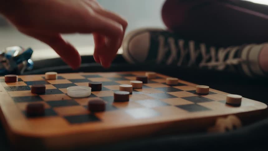 Two people playing checkers on a wooden checker board