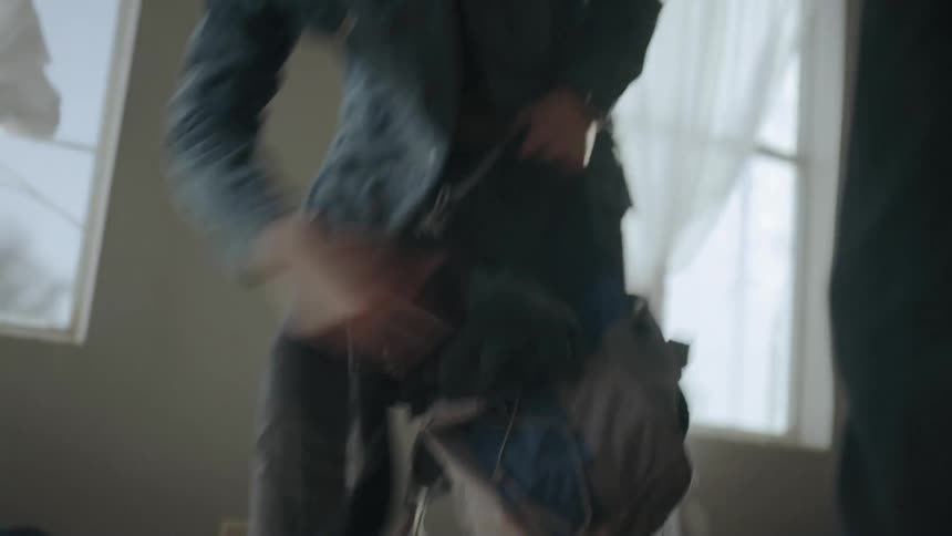 A person quickly shoves clothes into a bag in front of another person